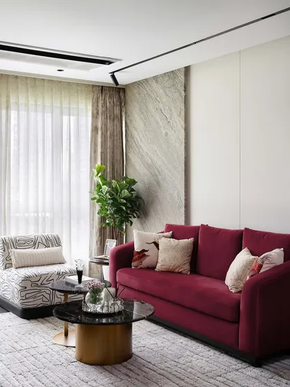 This living room corner showcases a bold ruby red sofa, which adds a vibrant pop of color against the neutral marble and white walls. The patterned armchair provides a stylish contrast.