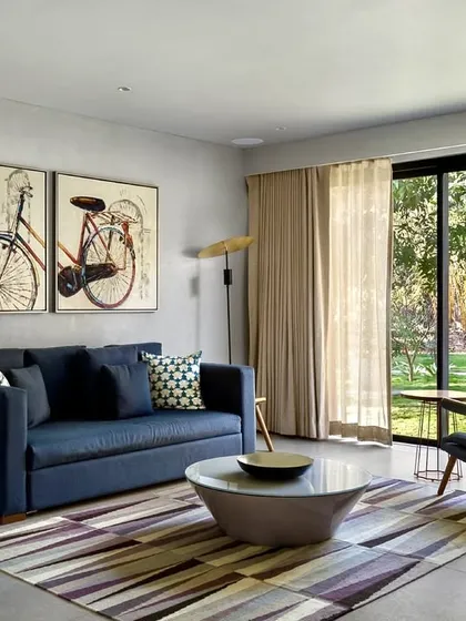 A cozy seating area in the Mango Orchard House offers a quiet corner for relaxation. The design combines modern furniture with traditional art, all while maintaining a direct visual connection to the lush green lawn outside.