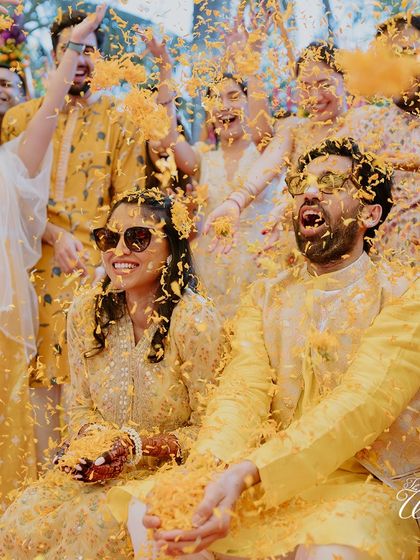 The whole group gets in on the fun. A wide shot of the couple and their friends enjoying a massive shower of marigold petals during the Haldi.
