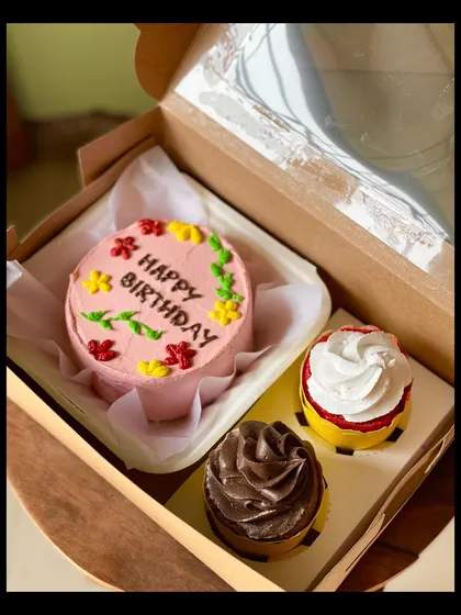 This colorful birthday combo includes a pink bento cake with floral decorations and two cupcakes, one chocolate and one vanilla. It's a perfect little party in a box.