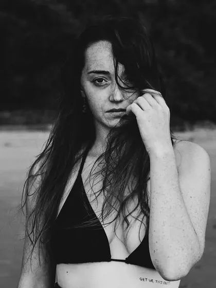 A raw and intimate black and white portrait taken on the beach. The natural setting and the subject's direct look create a feeling of authentic connection.