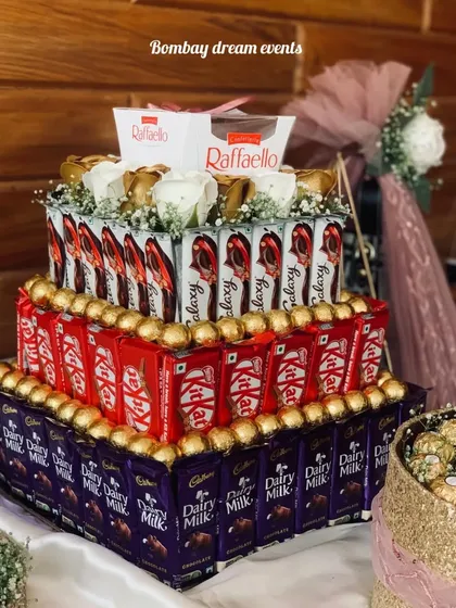 This luxurious four-tiered chocolate tower is the ultimate treat. It features layers of Dairy Milk, KitKat, Galaxy, and Ferrero Rocher, and is topped with white roses and a box of Raffaello.