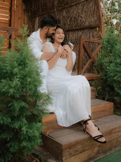 A moment of pure, uninhibited laughter on a rustic wooden porch. Dressed in coordinated white, this couple's joy is infectious, showcasing a perfectly candid moment from their pre-wedding shoot.
