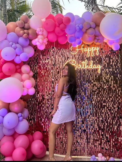 A beautiful birthday girl posing in front of a vibrant balloon wall with a sequin backdrop, in shades of pink and purple.