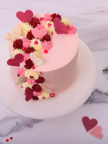 This romantic anniversary cake is a cascade of love, adorned with pink, red, and white chocolate hearts and delicate piping.