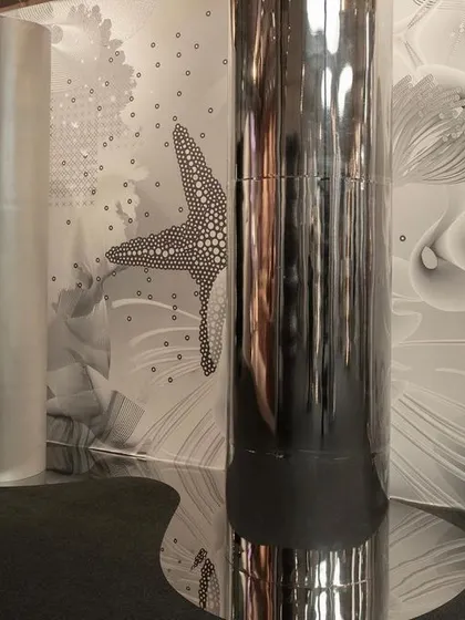 Reflective columns and a patterned wallpaper create a disorienting, futuristic environment in the 'Silver Escapade' installation. The space plays with illusion and perception.
