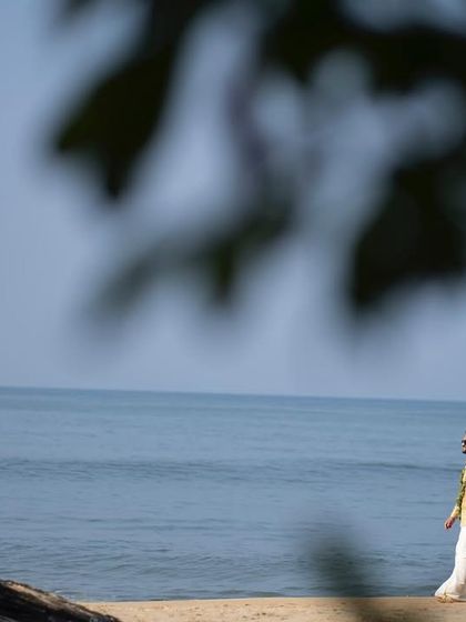 A beautifully framed shot of the couple walking along the beach, seen through natural foliage. This technique adds depth and an artistic touch to a classic beach walk photo.