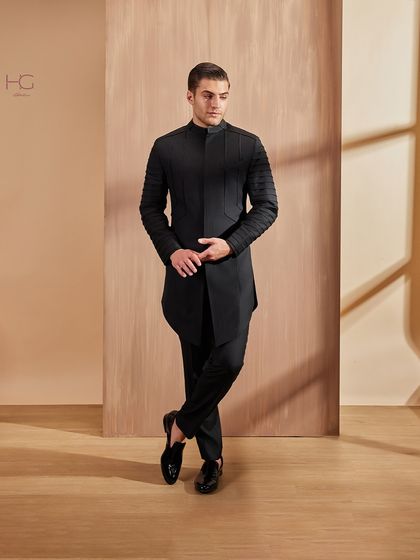 This pose highlights the architectural quality of the pleated sleeves and the asymmetric cut of the achkan, a fusion of classic tailoring and avant-garde design.