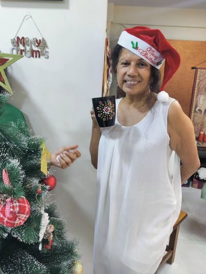 A guest wearing a Santa hat poses by the Christmas tree with the dot art mug she painted during the holiday celebration.
