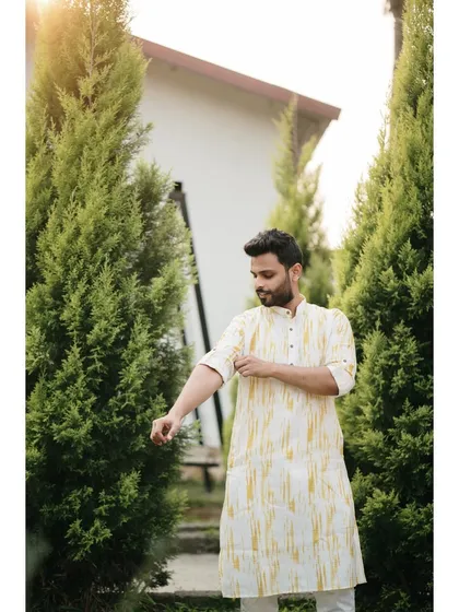 The groom getting ready for his Haldi ceremony. This candid shot, set against a row of green trees, captures a moment of quiet preparation.