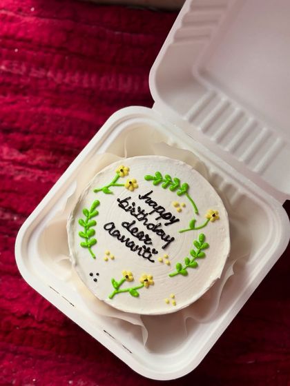A beautiful and minimal birthday cake with delicate greenery and tiny yellow flowers piped around the message "happy birthday dear Aavanti."
