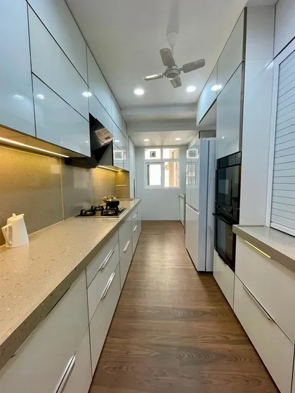 This long parallel kitchen uses a light color palette and wooden flooring to create a warm and inviting atmosphere. The layout includes floor-to-ceiling storage to maximize space.