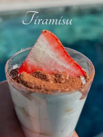 A classic Tiramisu cup, dusted with cocoa powder and topped with a fresh strawberry slice. A simple, elegant, and always delicious dessert, perfect for any occasion.