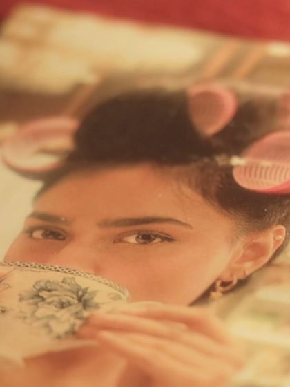 A creative and moody shot of a model with her hair in rollers, sipping tea, channeling main character energy for our "Summer Edit" campaign.
