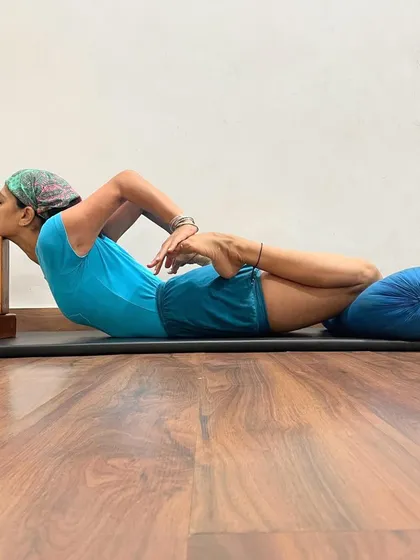 Bhekasana (Frog Pose) is shown here with props for support. A bolster under the abdomen and blocks for the head allow the practitioner to work on the deep quadriceps stretch without straining the lower back.