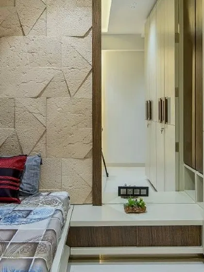 This compact bedroom design cleverly uses a textured stone wall and a mirrored wardrobe to create a sense of space. The raised bed platform includes built-in storage underneath.