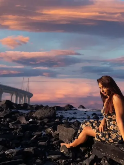 The model sits among the rocks by the Mumbai sea, looking down as the stunning sunset creates a dreamy and picturesque backdrop.