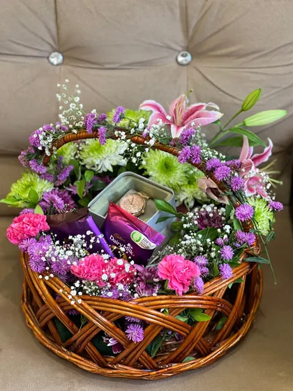 A basket overflowing with blooms is always a good idea. This rustic wicker basket is packed with a lush arrangement of pink carnations, purple statice, green chrysanthemums, and baby's breath, with chocolates and a watch box nestled inside for a beautiful surprise.