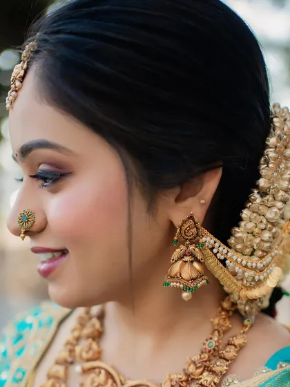 A side profile showing a classic South Indian bridal hairstyle. The hair is pulled back into a neat bun, adorned with fresh flowers and a traditional hair accessory.