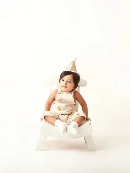 One of the adorable twin brothers posing for his first birthday portrait in a classic, neutral outfit.