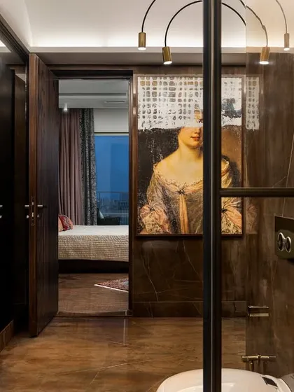 A view from the master bathroom into the bedroom, inspired by vintage elegance. The space features a striking piece of art and delicate hanging lights, offering a moment to restore and indulge.