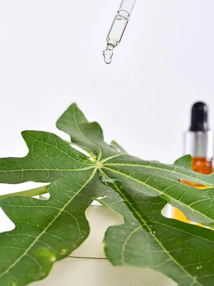 An artistic macro shot focusing on a drop of serum from a pipette, with a papaya leaf in the foreground. This image creatively highlights the product's natural ingredients and texture.