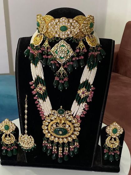 A stunning bridal set combining a wide choker with a long, beaded necklace. The design features green and pink stones, offering a vibrant and traditional look for any bride.