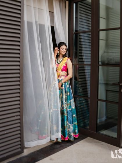 A beautiful solo portrait of the bride-to-be in her colorful lehenga, standing by a window. The soft, natural light highlights her happy expression and intricate outfit.