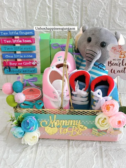 Another angle of the gender-reveal hamper, showcasing the arrangement of the plush elephant, colorful sign, and two pairs of baby shoes, all within a beautifully decorated basket.