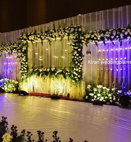 An engagement stage setup with elegant lighting and white floral arrangements, which can also serve as a beautiful photo corner near the entrance.