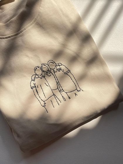 A clean shot of the finished line art embroidery on a beige sweatshirt, folded and ready to be loved. The simplicity is what makes it so beautiful.