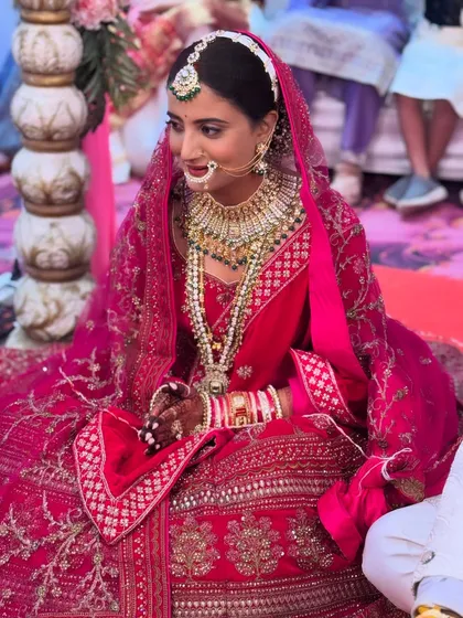 A candid moment from a North Indian wedding ceremony. The bride looks serene and beautiful in her red lehenga, with makeup that enhances her features without overpowering them.