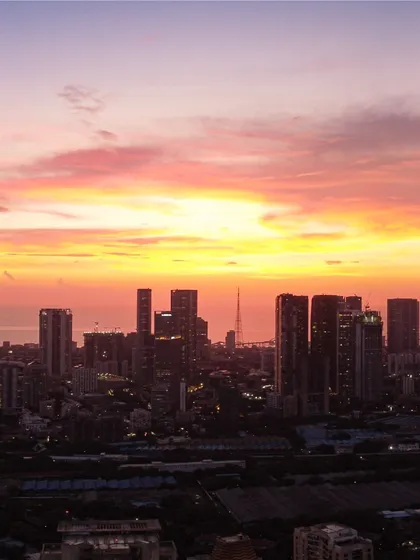 A beautiful shot of the Mumbai skyline silhouetted against a bright, fiery sunset, highlighting the density of the city's architecture.