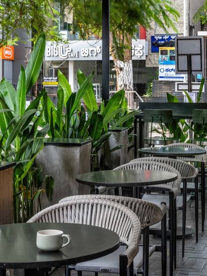The outdoor seating area is separated from the street by large planters filled with tropical plants, creating a green buffer that offers a sense of escape and tranquility in the middle of the city.