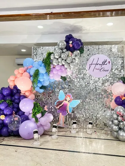 A fairy butterfly theme with a silver sequin wall backdrop. The purple, blue, and silver balloons create a mystical, enchanted forest feel.