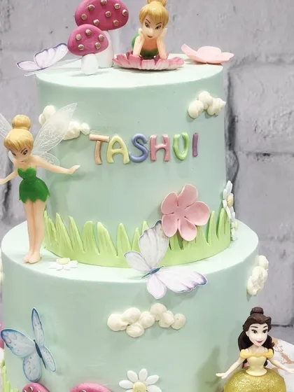 A close-up of the details on this Disney princess and fairy cake. Every element, from the tiny flowers to the character toppers, is placed with care to create a story.