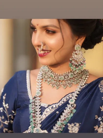 A smiling bride, her makeup featuring a bold red lip and defined eyes that stand out beautifully with her silver and mint green jewellery.