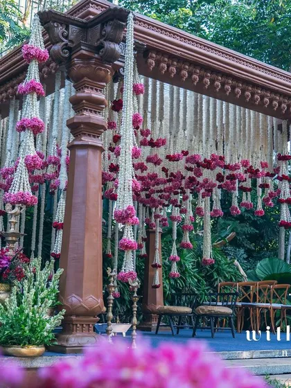 A traditional South Indian wedding mandap adorned with fragrant tuberoses and pink oleanders. The floral garlands cascade from intricately carved wooden pillars, creating a sacred and breathtaking space for the couple to exchange their vows.