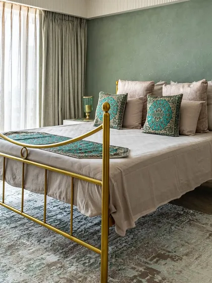 The 'Eternity' master bedroom, with its beautiful gold-finished metal bed frame and sage green accent wall. The design blends modern lines with traditional Indian textile patterns.
