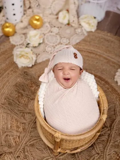 A sleepy yawn from a newborn tucked into a wicker basket. The neutral tones of the swaddle and the rustic jute rug create a warm, bohemian-inspired setting.