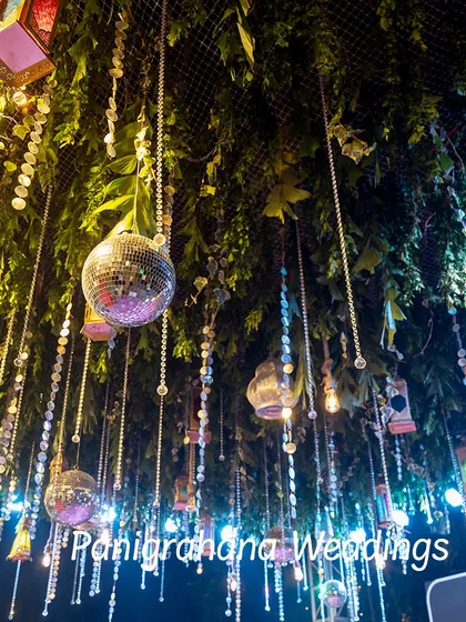 A view of a ceiling decorated with greenery, disco balls, and hanging lanterns, creating a multi-layered and festive look for a Haldi celebration.