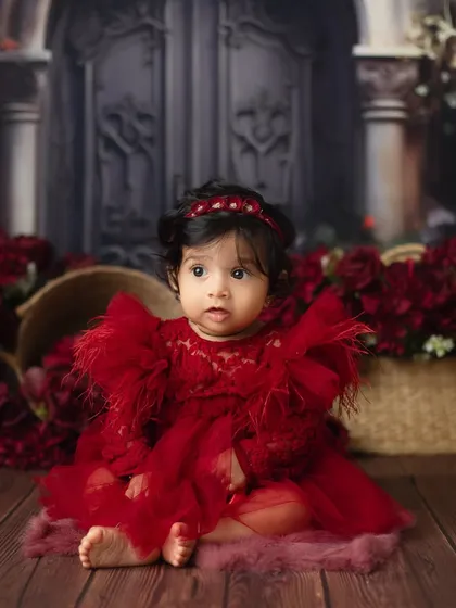 A beautiful baby girl in a stunning red dress. The deep red flowers and dark background create a dramatic and painterly portrait.