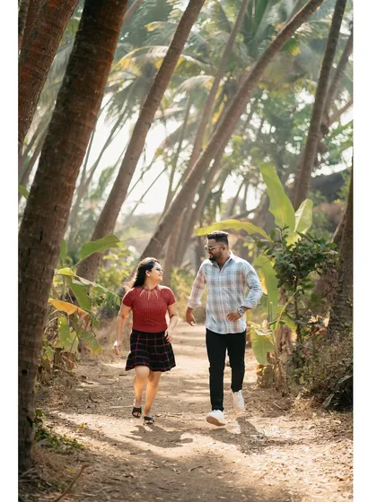 A candid shot of the couple walking and talking on a path lined with palm trees, capturing their natural interaction.
