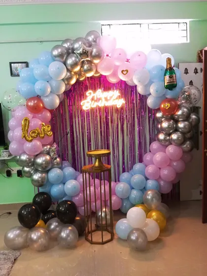 A playful and colorful birthday setup with a mix of pastel pink, blue, and chrome silver balloons on a circular frame. Foil balloons like a champagne bottle and the word 'love' add a fun, celebratory feel.