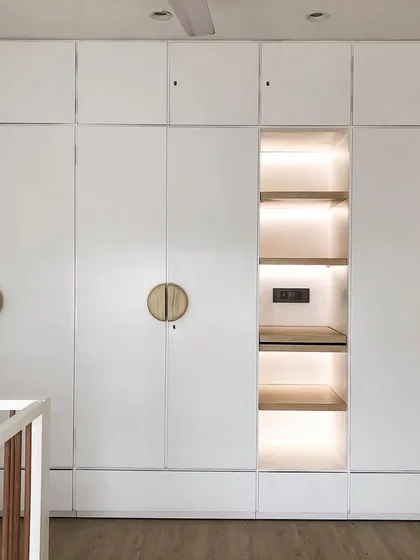 This custom white wardrobe features a lit-up central niche, perfect for displaying special items or for use as a small changing station. The round wooden handles add a soft, modern touch.