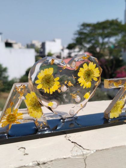 A personalized resin initial frame, perfect for couples. This piece features the initials 'A' and 'Z' with a heart in the middle, all filled with preserved yellow flowers and set on a sleek black base.