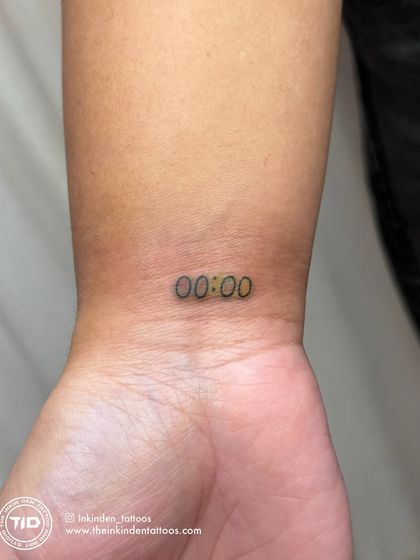 A clear look at the final corrected "00:00" tattoo. The lines are now sharp, and the color is even, transforming a faded mark into a crisp and meaningful piece on the wrist.