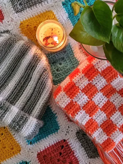 A cozy scene featuring some of my handmade crochet work. This picture shows a colorful granny square blanket, a striped grey and white beanie, and a checkered orange and white scarf. It’s a little glimpse into the comfy and stylish pieces I love to create for chilly weather.