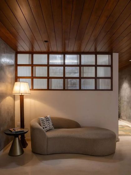 A comfortable chaise lounge sits under a wooden ceiling, with a traditional fluted glass screen providing a sense of privacy.