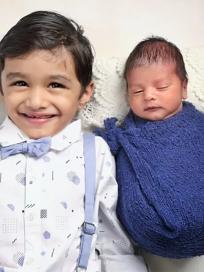 A big brother's beaming smile says it all. This shot captures the pure joy and excitement of welcoming a new baby into the family, with the newborn swaddled safely in blue.